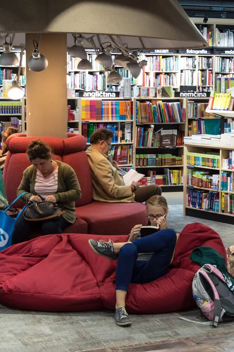 Tentang Kami A welcoming library space with people relaxing and reading on comfortable seating.